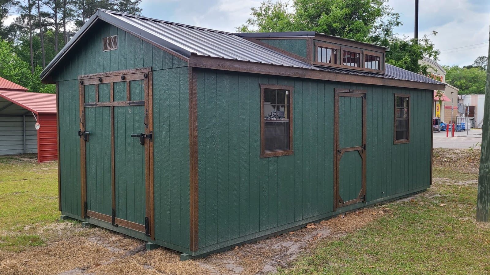 A 12x24 green portable building with brown trim and a dormer on the Wiggins Best lot in Walterboro, SC